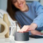 Mulher deitada de lado na cama apertando a alexa que está na mesa ao lado
