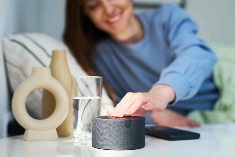 Mulher deitada de lado na cama apertando a alexa que está na mesa ao lado